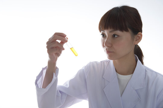 黄色の薬品の入った試験管を見つめる女性研究員