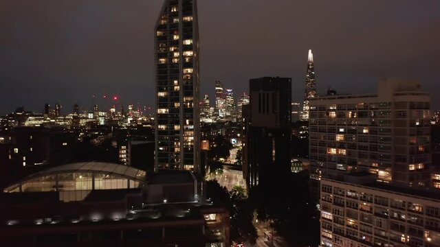 Forwards fly above glowing street around tall residential buildings. Revealing night cityscape. London, UK