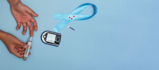 Close up top view of concept for World Diabetes Day 14 November. Child measures blood sugar on a blue background, and a blue ribbon with blood drops