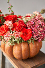 Flowers arrangement in pumpkin on wooden table. Fresh cut flowers for decoration home. European floral shop. Delivery fresh cut flower.