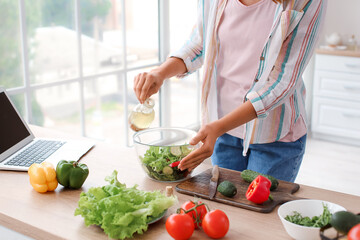 Young woman preparing fresh vegetable salad in kitchen