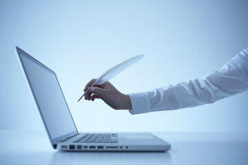 青い背景に置かれたノートパソコン羽根を持つ手