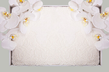Milky beige and lilac towel with lace in a box on a fly-olive background with an orchid branch.