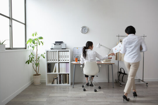 椅子に座る女性に資料を渡す女性