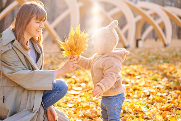 Portraits of a cute 1 year old baby girl and her young mother. Walking in Yellow Autumn Park. Leaf fall and yellow leaves. sunny day