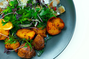 Fototapeta na wymiar Country style fried potatoes with herring on a black plate.
