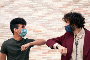 Young multiethnic men wearing masks greet each other by bumping elbows as a preventive measure to...