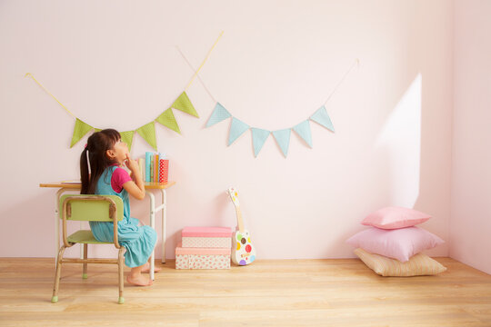 ピンク色の壁の子供部屋で勉強机に座っている女の子