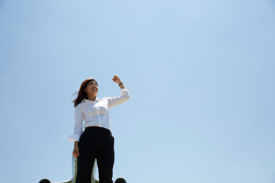 青空をバックにガッツポーズをしている白いブラウスの女性