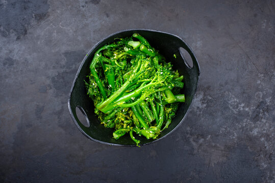 Frischer Rapini Broccoli Rabe mit Sesam als Draufsicht auf eine schwarze Schale mit Textfreiraum