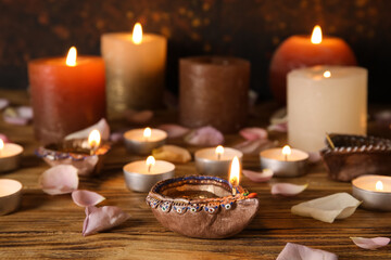 Diya lamp for Diwali, candles and flower petals on wooden table