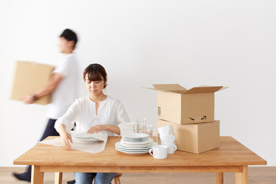 食器を梱包する女性と、ダンボール箱を運ぶ男性