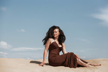 Fototapeta na wymiar Dark brunette with voluminous curly hair among the Sands in a sand dune in a flying dress