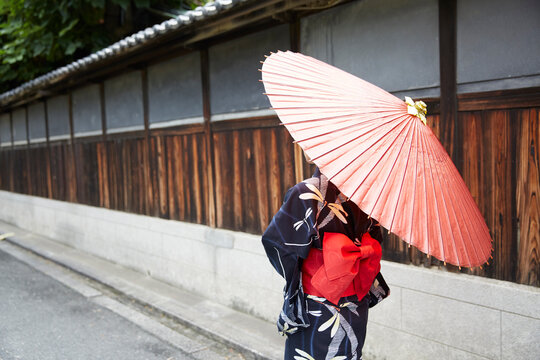 日本家屋の横を、和傘をさして歩く浴衣の女性