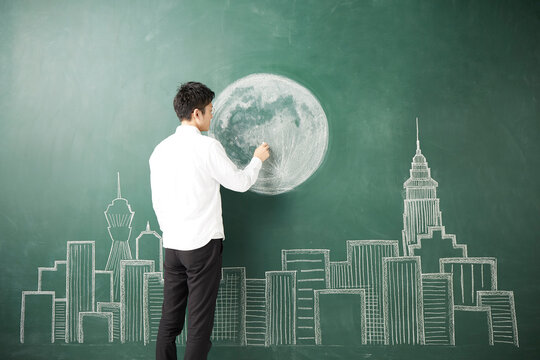 ビル群が描かれた黒板に満月のイラストを描く