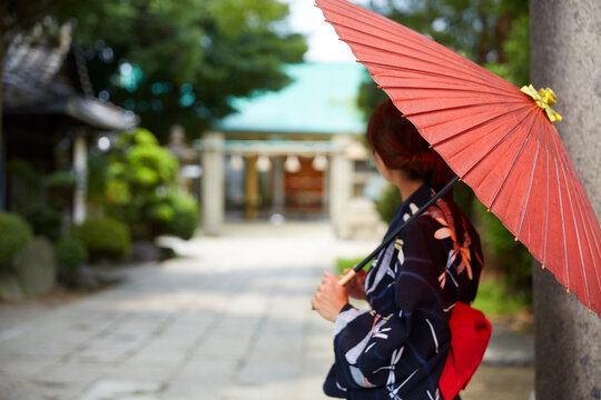 神社の参道に立つ、傘をさした浴衣の女性