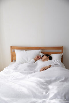 明るい光の入ったシンプルなベッドルームと眠る男性