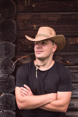 Young man in a cowboy hat on the background of a wooden log house.