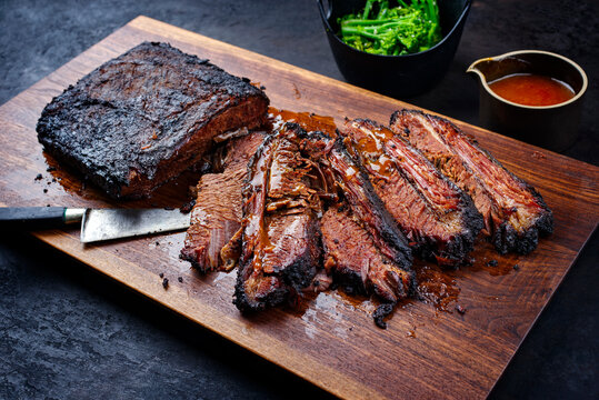 Modern style traditional smoked barbecue wagyu beef brisket with baby broccoli served as top view on a wooden design cutting board with Louisiana sauce