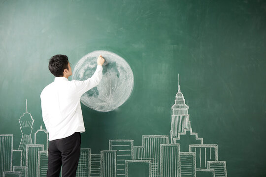 ビル群が描かれた黒板に満月のイラストを描く