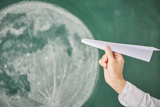 満月が描かれた黒板イラストの前で紙飛行機を飛ばす