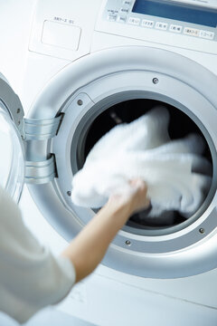 ドラム式洗濯機に洗濯物を入れる女性の手