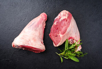 Raw traditional lamb shank with herbs offered as top view on a black board with copy space - obrazy, fototapety, plakaty