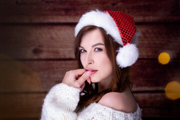 Fashion young beautiful brunette woman with dreamy look.  X-mas concept, woman portrait with santa cap and  knitted sweater isolated wooden background.