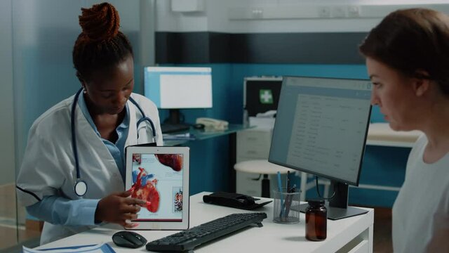 African american doctor showing cardiovasular image on tablet to patient for cardiology diagnosis. Black medic explaining heart condition and blood flow to young person with gadget