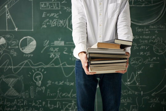 黒板の前でたくさんの本を持つ