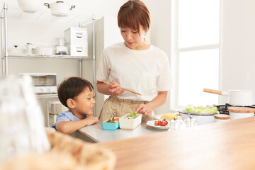 キッチンでお弁当を作る女性と寄り添う男の子