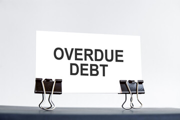 a white card with overdue debt text stands on paper clips on a desk against the light blue...