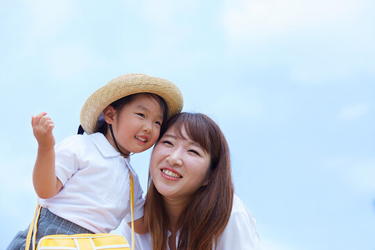 青空を背景に頬を摺り寄せて笑う母と子
