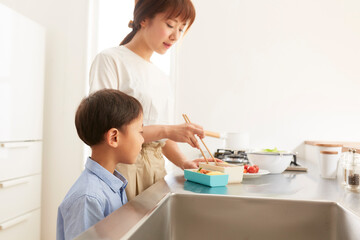 キッチンでお弁当を作る女性と寄り添う男の子