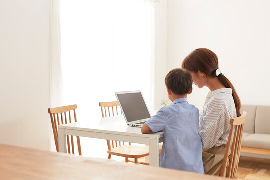 ダイニングテーブルで在宅ワークをする女性のパソコンを覗く男の子