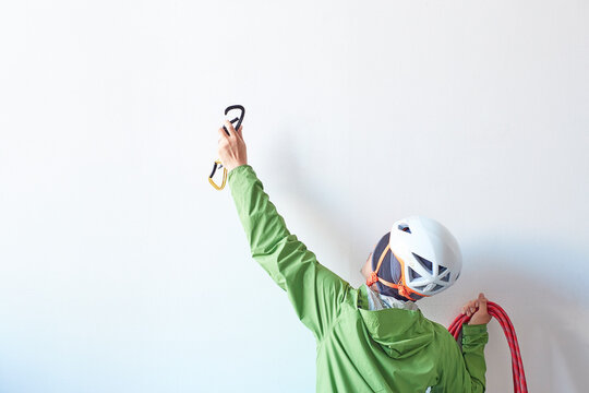 白い壁の前でロープを持ち体を伸ばしてカラビナを引っ掛けようとする登山者