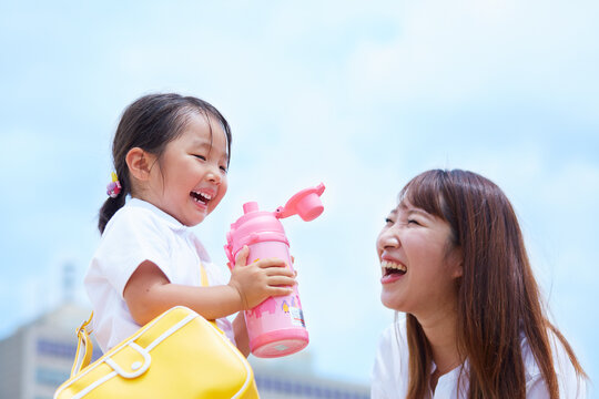 青空を背景に水筒の飲み物を飲む子と見つめる母