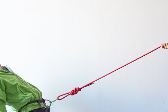 白い壁の前でカラビナがかかったハーネスを引っ張られる登山者