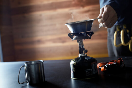 山小屋の中の机でガスコンロを使い飲み物を温める人