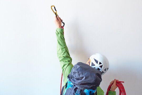白い壁の前でロープを持ちカラビナを引っ掛けようとするリュックを背負った登山者