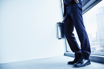 アタシュケースを持つ窓辺に立つ男性の足元と床