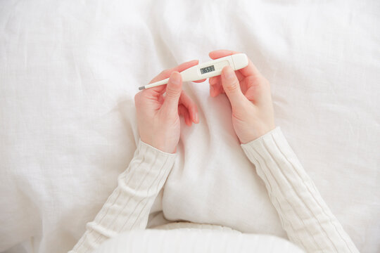 ベッドの上で体温計持つ女性の手元