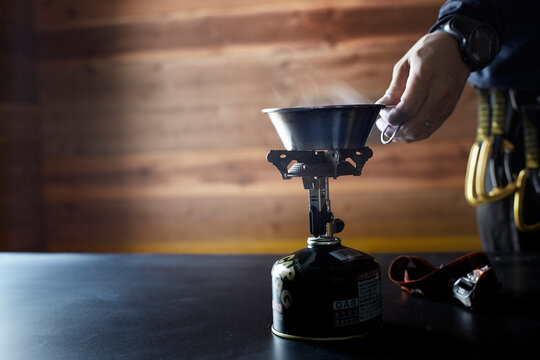 山小屋の中の机でガスコンロを使い飲み物を温める人