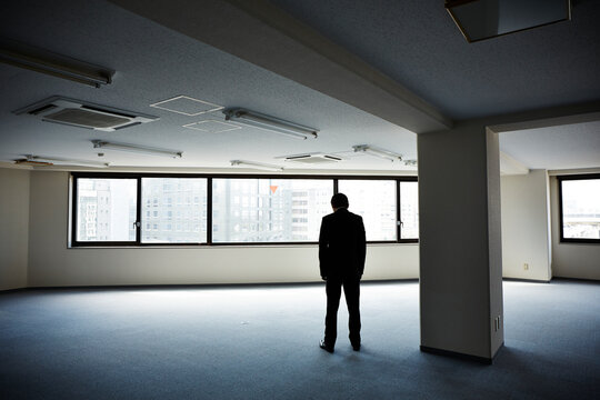 何もないオフィスで下を向き立ちすくむ男性