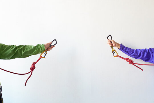 白い壁の前でロープを持ちカラビナを引っ掛けようとする２人の登山者