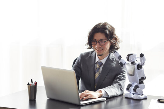 ロボットとパソコンを見るスーツを着た男性