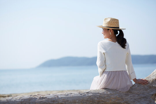海辺の流木に座って海を眺める女性 ,日本,和歌山県,和歌山市,加太周辺