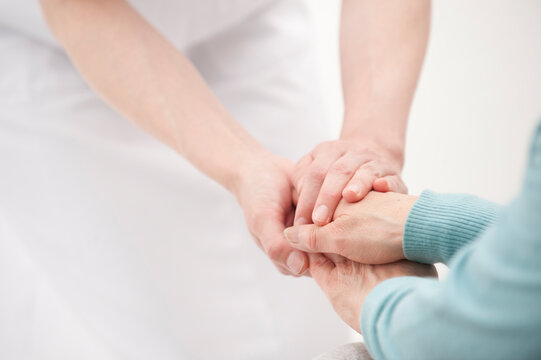 車椅子の老人女性の手を握る看護師の手