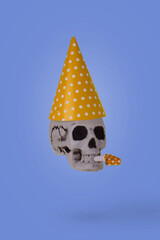 Human skull  with a yellow birthday cap and whistle isolated on a purple background.