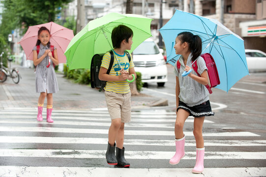雨天の登下校で傘をさした小学生子供男女3人